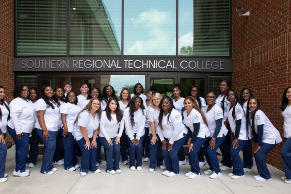 Practical Nursing students in scrubs pose outside brick building