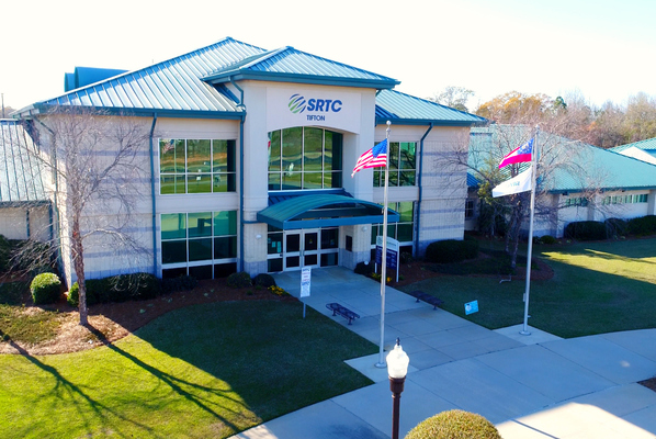 Aerial view of SRTC Tifton's Building A entrance, tan brick with teal roof, American and Georgia flags flying near the walkway.