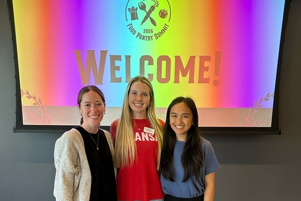 Three attendees stand together in front of a welcome screen.