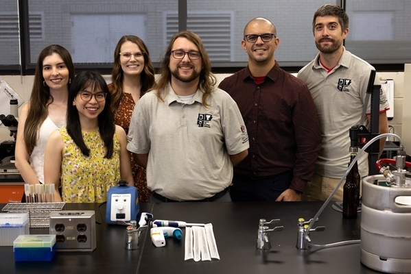 Students and professors stand together in lab. 