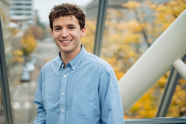 Student poses for picture in front of window with a tree outside with yellow leaves. 