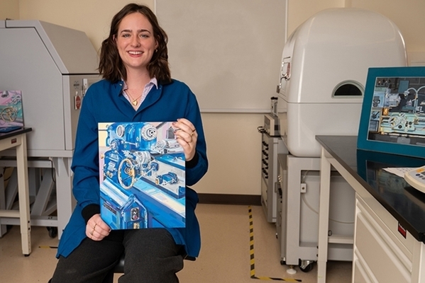 Student sits in chair holding her artwork in an engineering lab