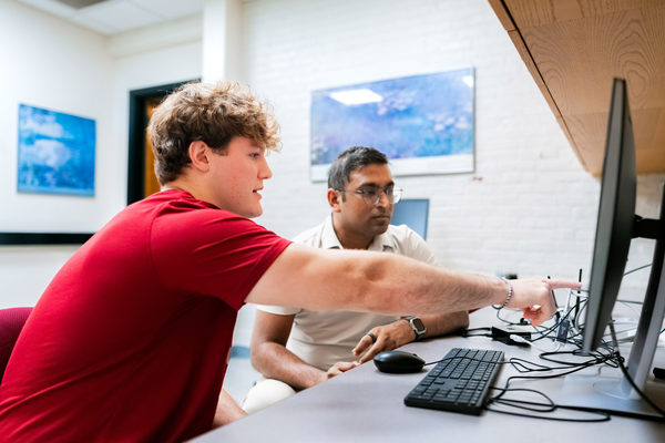 Thomas Cerruti looks at a computer with his computer science mentor Proyash Podder.