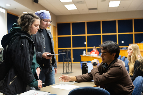 Students standing in front of a desk as another student checks them in.