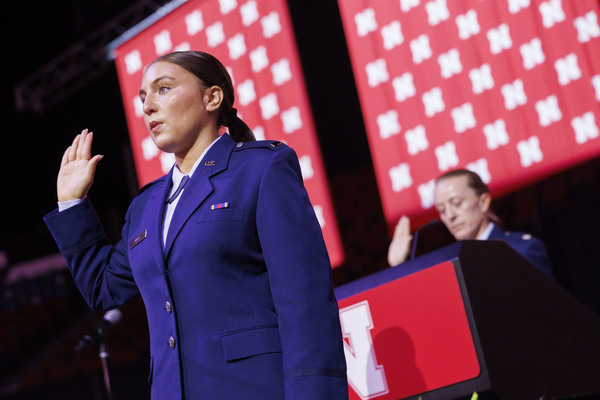 A young woman in an Air Force dress uniform holds her right hand up as she recites an oath. A female officer reads at a lectern in the background.
