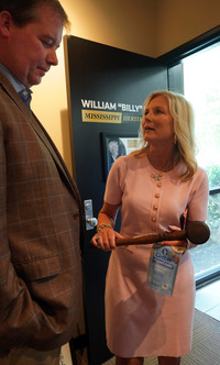 Kimberly holds a wooden gavel while speaking with a guest near the entrance to the William “Billy” McCoy Mississippi Heritage Room.