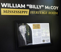 Entrance signage identifies the William “Billy” McCoy Mississippi Heritage Room above a framed display containing McCoy’s portrait and biography.