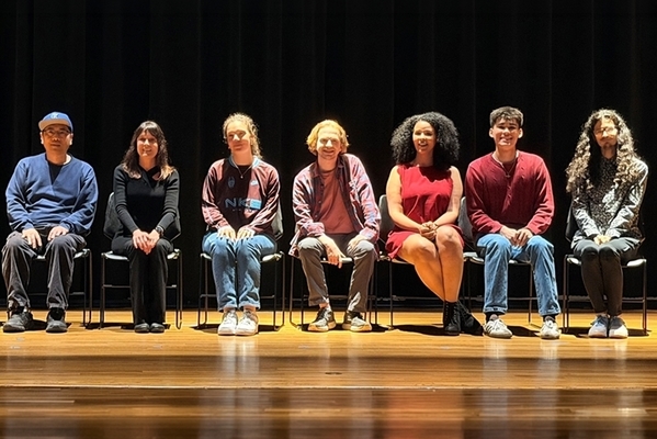 students sit in chairs on a stage with their professor