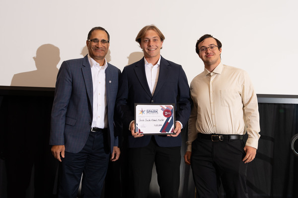 Three people standing together, with the middle person holding an award certificate.