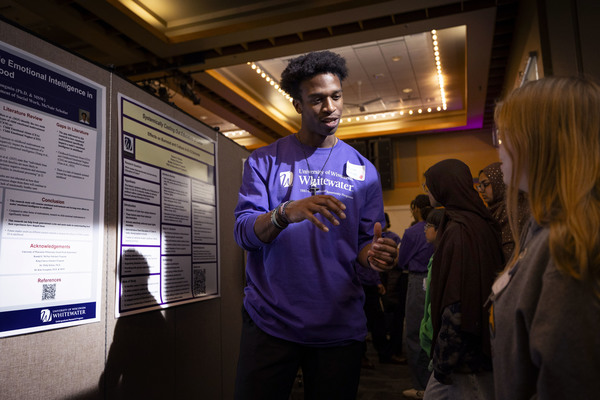 A college student presents a poster to people on a college campus.