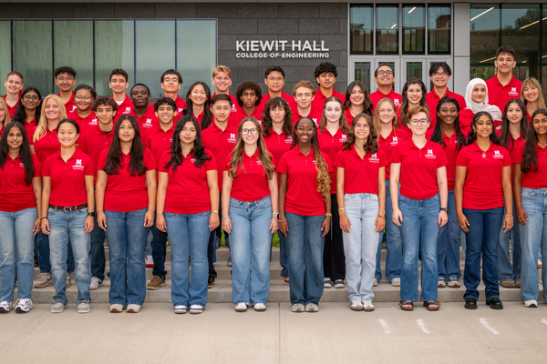 Forty University of Nebraska–Lincoln students in red polos and blue jeans pose for a group photo in front of Kiewit Hall.