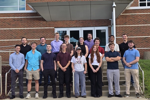 12 new members of Kettering University's Mechanical Engineering International Honor Society Stand in front of a brick building on campus.  