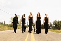 Seraph Brass walk down the street holding their instruments, wearing formal black gowns.