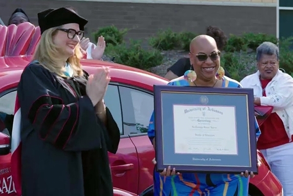 student holds framed degree from the University of Arkansas in front of Razorbug car