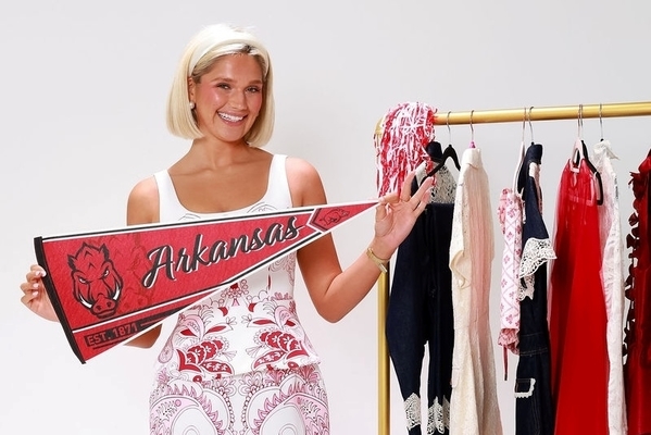 Student stands in front of rack of clothes holding an Arkansas pendant