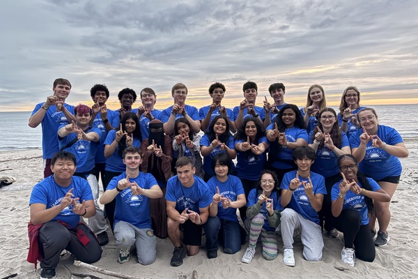 UB students doing the horns up sign on the beach.