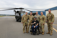Man in wheelchair shown with helicopter crew and UH-60 in the background.