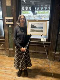 Iggy Beerbower stands near her framed photograph, which shows a woman facing toward the ocean on a beach.