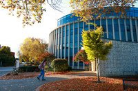 A person walking a path with a circular building in the background and fall foliage.