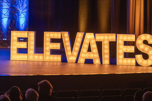 White letters three feet high spelling ELEVATES shine with yellow lights on the darkened stage of the ETSU Martin Center for the Arts.