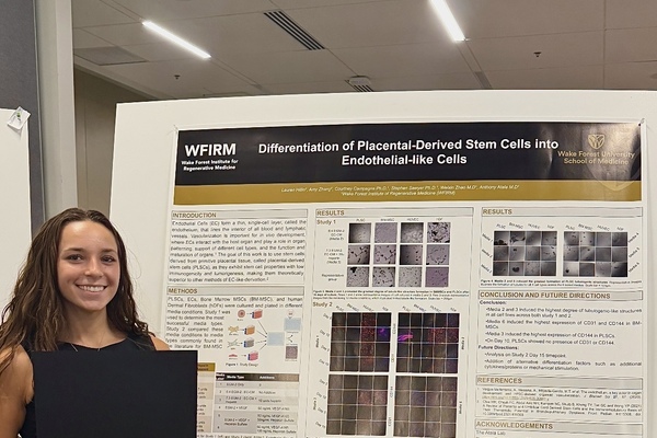 Female student holding certificate, standing in front of research poster