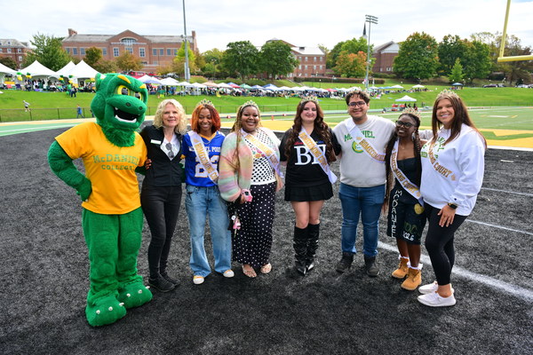 The McDaniel College 2026 Homecoming Court standing in a row smiling for a picture with the Green Terror and McDaniel College President Julia Jasken.