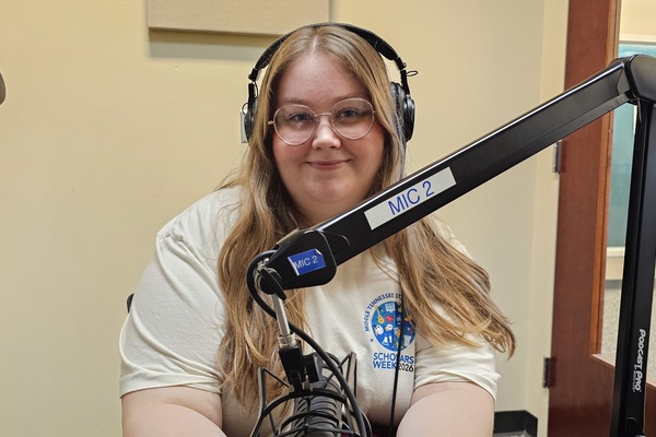 woman with glasses sits in front of microphone wearing headphones