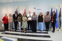 A diverse group of men and women in professional clothing pose with a wooden plaque.