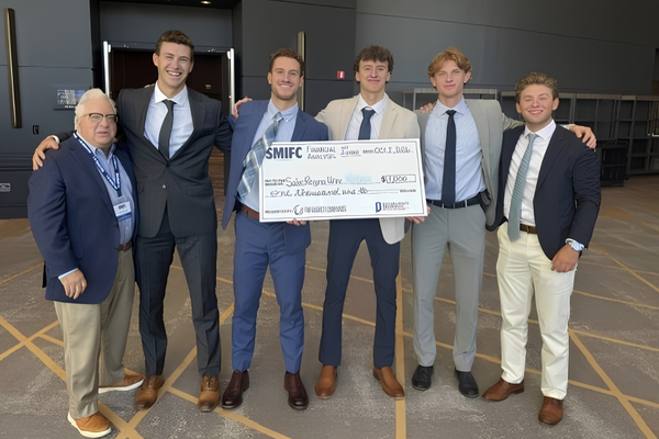 Professor and five male students posing with oversized check