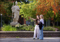 Two students stand together at Minerva Plaza. One is pointing while talking to the other one.