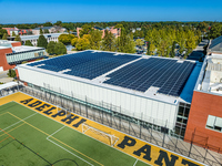 Closer shot of a modern campus building and athletics field with solar panels on the roof.