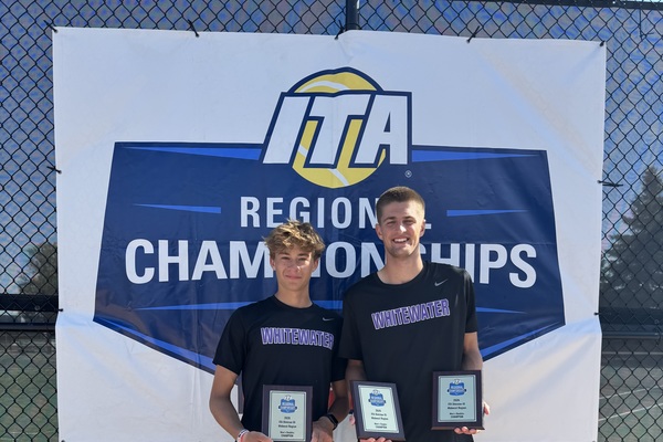 Two tennis players standing with first-place plaques in front of a banner.