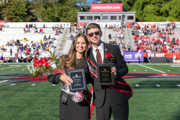 SEMO's 2026 Man and Woman of the Year, Kaelee Karcher and Blake Deppe smile on the football field as they hold their awards.