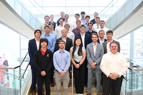 Twenty-five men and one woman — all in professional attire — pose for a group photo on a staircase in Howard L. Hawks Hall.
