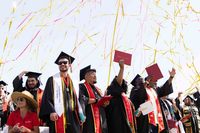 Stanislaus State graduates in caps and gowns celebrate as red and gold streamers fill the sky above them.