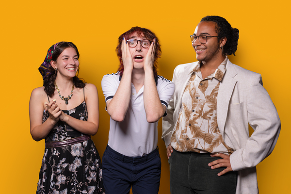 Three students pose against a yellow backdrop