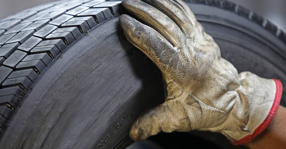 A close-up of a hand wearing a dirty, distressed, white leather glove over the smooth sidewall of a tire.