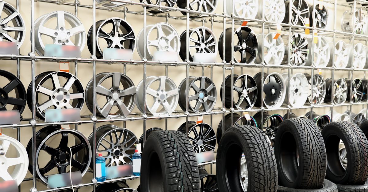 A display rack holds many rows of wheels in various designs and materials. Car tires are on display in front of the rims.
