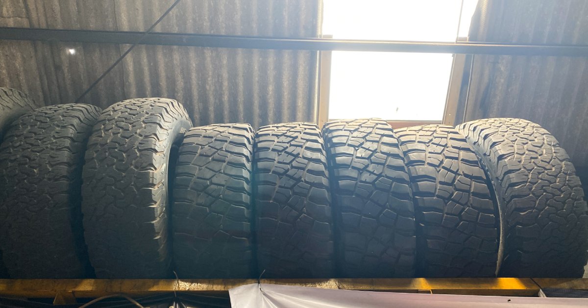A ground view looking up at a row of used all-terrain automotive tires stacked vertically on the top shelf.