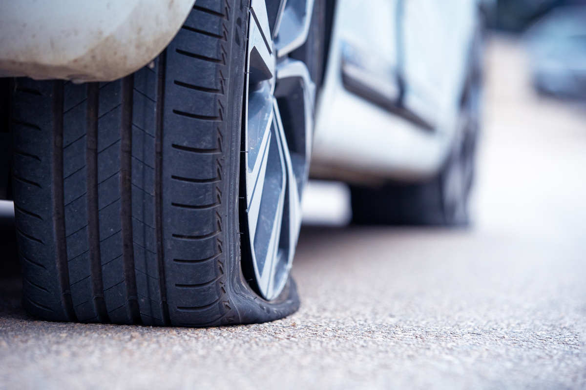 A close-up of a rear right automotive tire of a silver four-door vehicle deflated completely on the pavement.