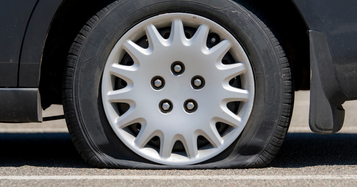 A close-up of a vehicle's tire that's flat. The car is parked at a parking lot between the white lines.