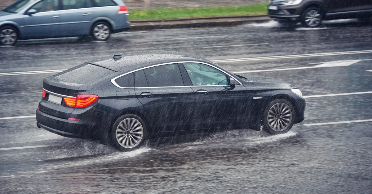 A car driving fast on a wet road, splashing through puddles in the rain alongside other cars going the opposite direction.