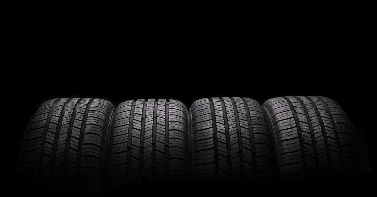 A close-up of four large, brand-new automobile rubber tires spotlighted and isolated on a black background.