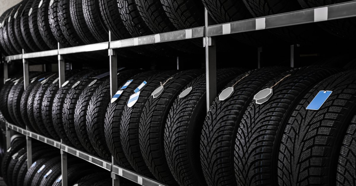 A close-up of multiple car tires on a rack in an automotive store. The brand-new tires have price tags on them.