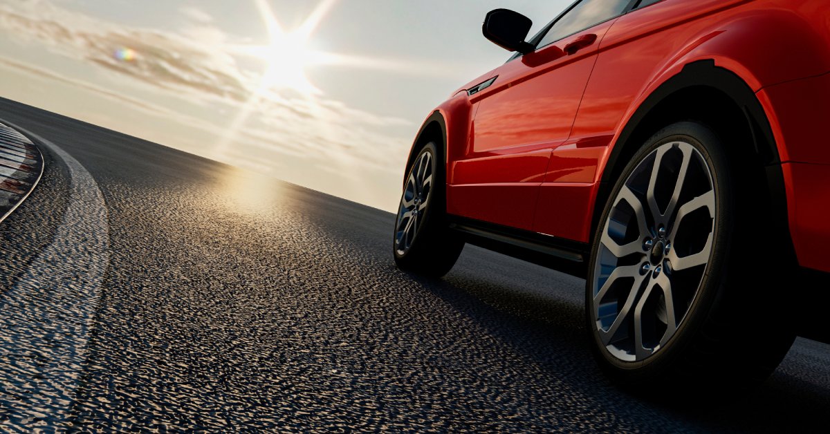 A close-up of a red car sedan with tinted windows and brand new tires riding on the road into the sunset.