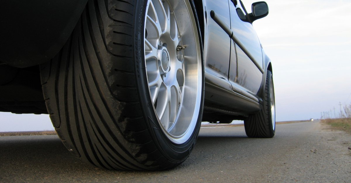 A car's rear passenger tire, up close. The steel rims are bright, and the tire has a bit of dirt on it.