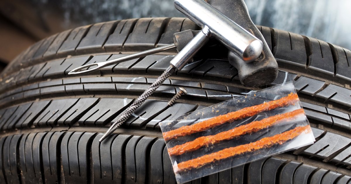 A tire with a flat tire repair kit lying on top of it. Some of the tools are a plugger, a pressure gauge, and a plug.