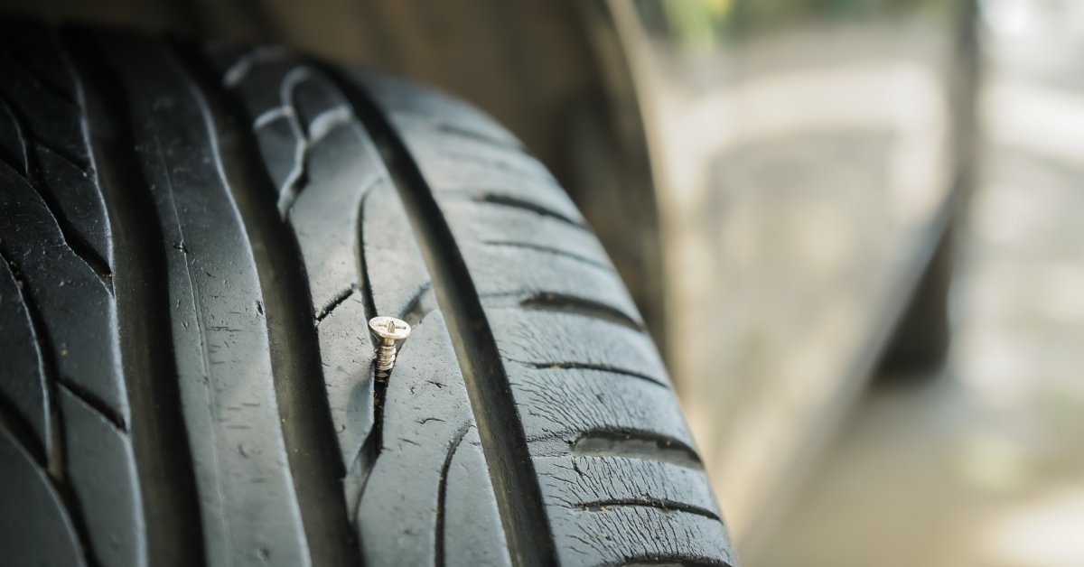 A nail embedded in the treads of a tire that has scuff marks along the edge of it. The tire looks worn from driving.