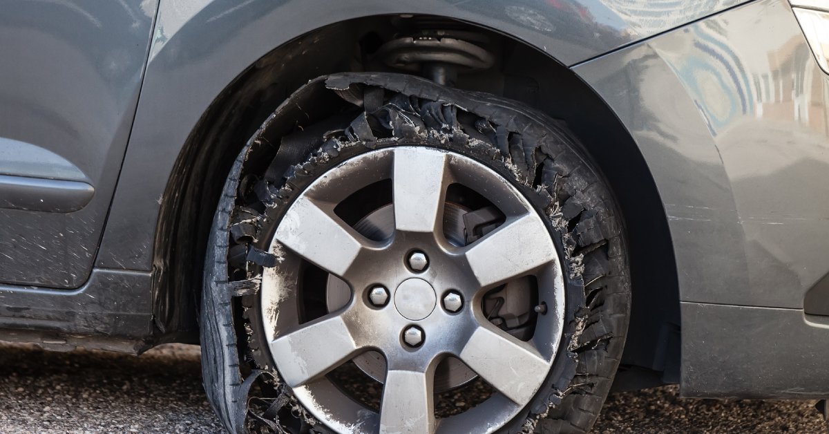 A destroyed tire on a vehicle with the rubber shredded and the rim close to the ground.