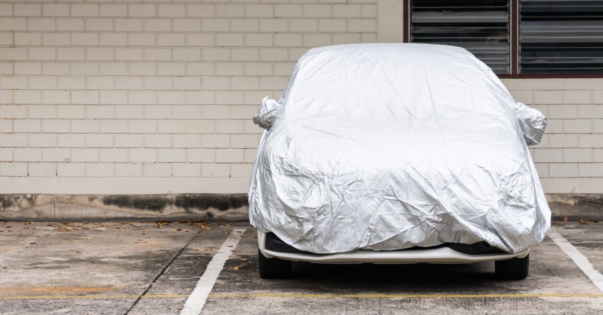 Outside of a building with wooden bricks, a car is in a parking spot. A silver cover covers the vehicle.